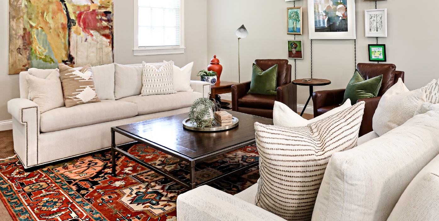 Contemporary living room with neutral sofas, leather chairs, colorful rug, and modern art wall.