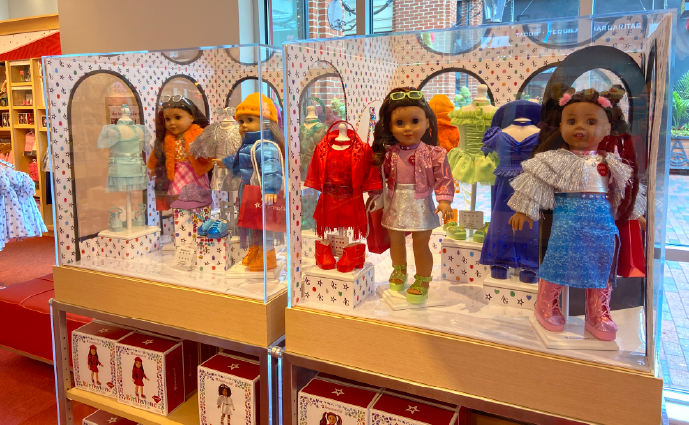 diverse-doll-collection-cases Diverse doll collection displayed in clear acrylic cases wearing colorful outfits including red coat, pink jacket, and blue ensemble